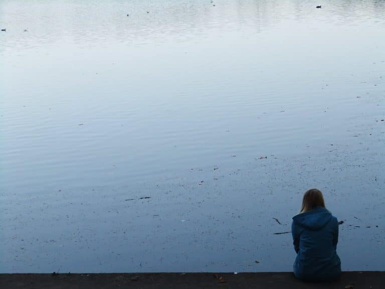 Frau allein am Wasser sitzend