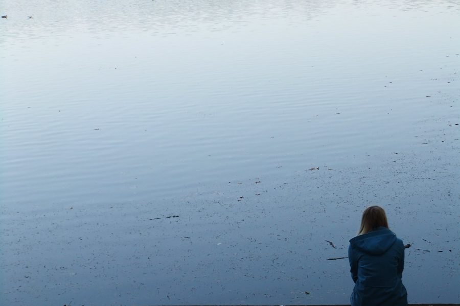 Frau allein am Wasser sitzend